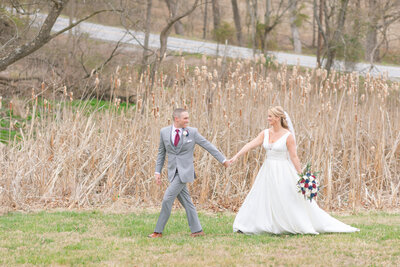 husband and wife walking through field on wedding day