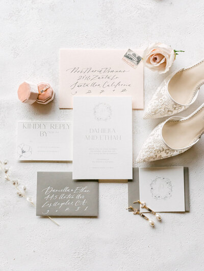 Flatlay of wedding invitation, rings, jewelry, and heels