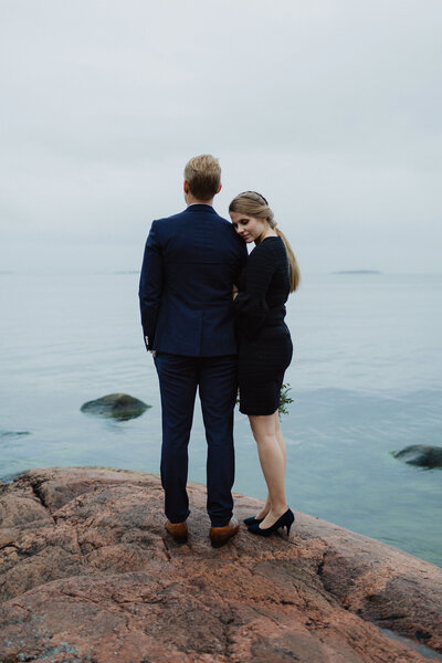 Nainen nojaa päätään silmät kiinni miehen olkapäähän ja mies seisoo selkä kameraan päin katsoen merelle Lauttasaaressa Helsingissä