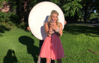 Behind the scenes female musician photoshoot Krista Earle wearing pink dress holding vintage microphone in front of white round reflector