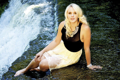 Musician portrait Krista Earle sitting by waterfall in wet white skirt and black blouse