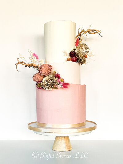 Pink and white three tiered cake on a marble cake stand. Cake has decorations at each tier.