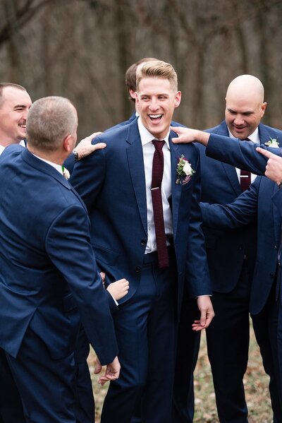 Groomsmen patting groom on shoulders and laughing together
