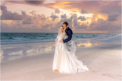 Bride and groom in wedding attire embracing on a Sarasota beach  at sunset.