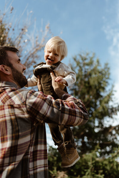 A dad tosses his young toddler boy in the air and bright spring sunshine outside