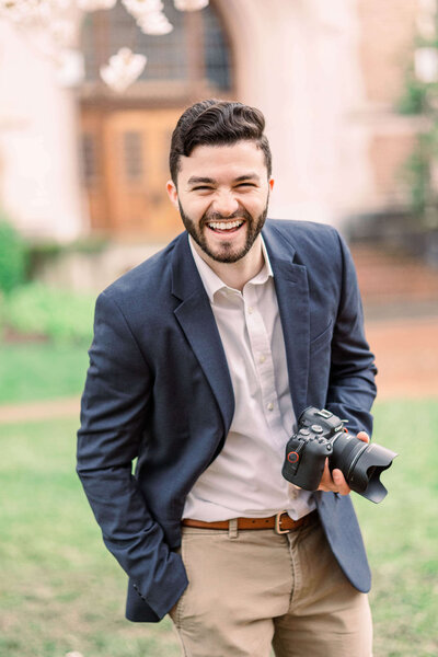 Jason Goldfarb photography holding his camera, laughing and leaning in towards the viewer