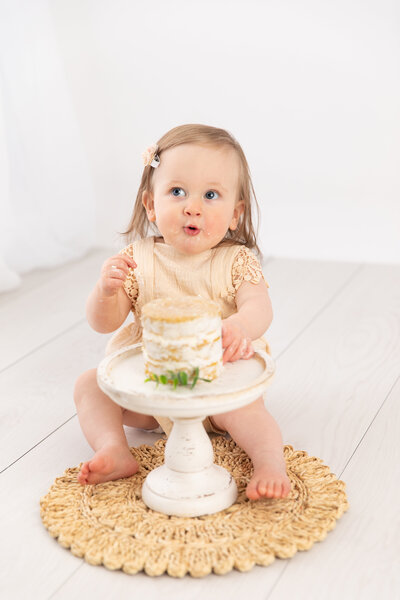 Baby girl in romper smiling while eating cake