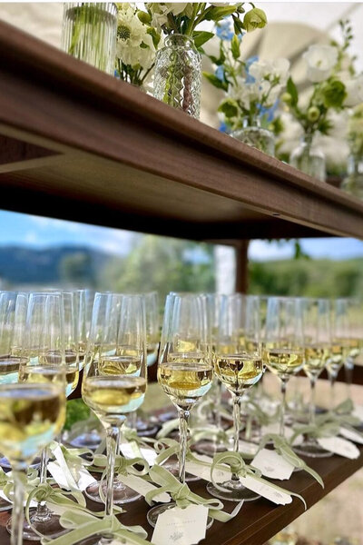 A champagne seating chart adorned with elegant crystal flutes and personalized escort cards tied with velvet ribbons on each glass guide guests to their seats for a summer wedding in Jackson, WY.