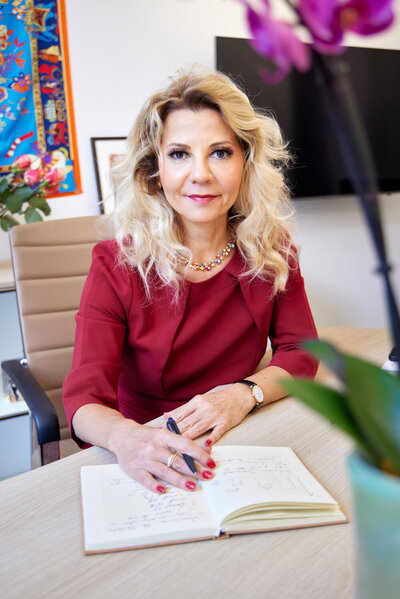 Roxana in a red dress sitting by the desk, taking notes in her office in Frankfurt