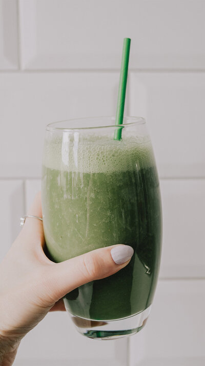 Someone holding a refreshing green smoothie in a clear glass.