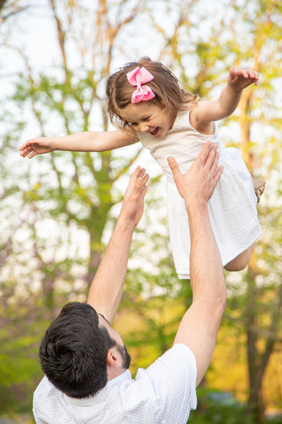 Dad tosses his young daughter in the air as she smiles during family photography session