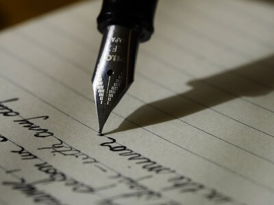A black, silver-tipped fountain pen writes in cursive across lined notebook paper.