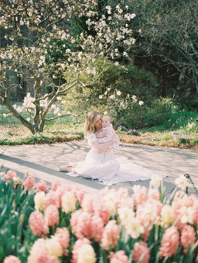 A blonde mother sits on a blanket with her baby girl in Brookside Gardens with tulips