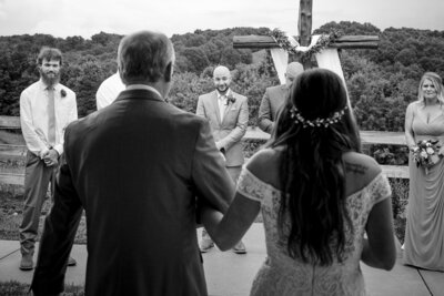 Black and white image of a groom seeing his bride come down the aisle shot between the father of the bride and the bride by Charlotte wedding photographers DeLong Photography