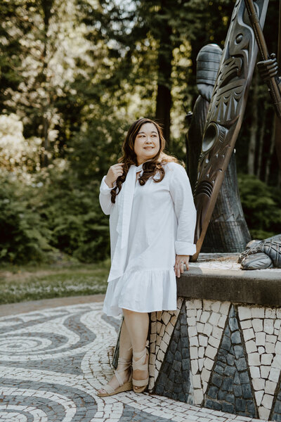 Anne @purposeinview Stanley Park looking over her right shoulder wearing a white dress from The Sleephshirt and photo by Flytographer.