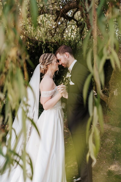 Bride and groom standing under willow tree