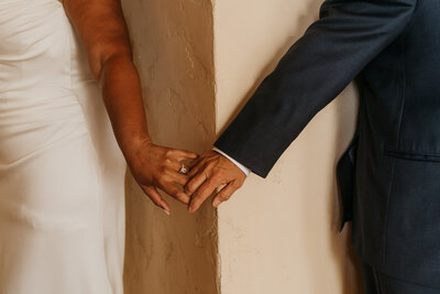 Two hands reaching around a corner to hold each other 