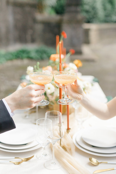 couple cheers pretty cocktails over detailed wedding reception table
