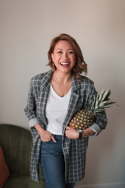 woman smiling with one hand in her pocket and the other holding a pineapple