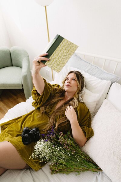 Capturing elegance: A girl in a stunning dress reclines on a bed in a photo studio, striking poses with a notebook