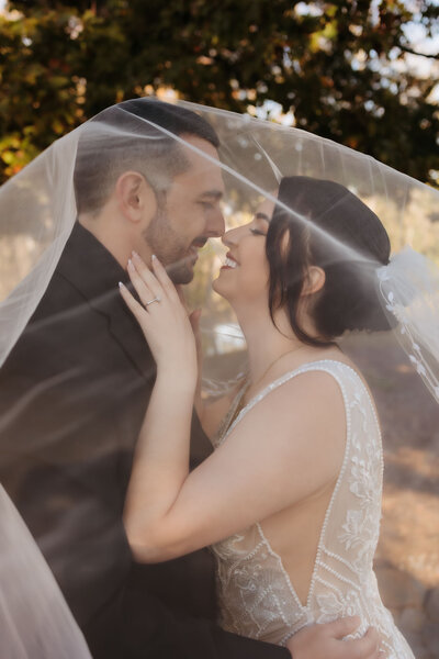 couple smiling under wedding veil
