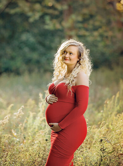 new jersey expecting mom wearing a form fitting red dress looking up and holding her belly