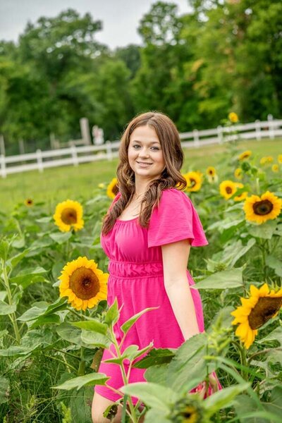 a young woman in a pink dress standing in a field of sunflowers