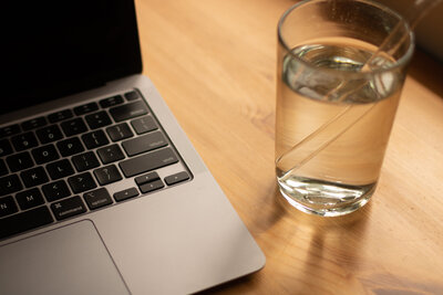 Portion of mac book and clear glass of water with clear straw