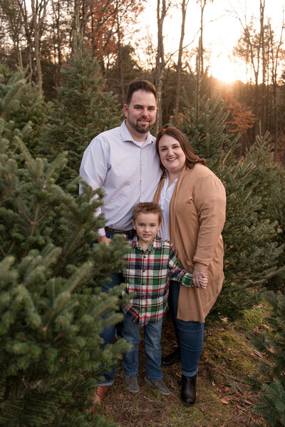 Family of three standing in front of a Christmas tree at sunset
