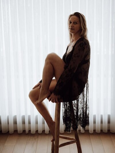 Vrouw in zachte ochtendjas kijkt zelfverzekerd in de lens tijdens boudoirshoot in Beveren.
