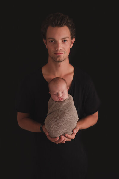 newborn baby wrapped with dad holding him with black background