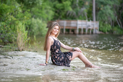 High school senior girl sitting at the edge of a river with her feet in the water by Orlando senior photographer Khim Higgins.