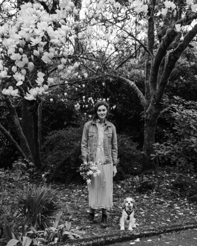 black and white photo of a a woman holding a bouquet of flower with a dog at her feet