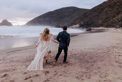 Destination elopement photographe captures couple running on the beach during their bridal portraits in Big Sur California