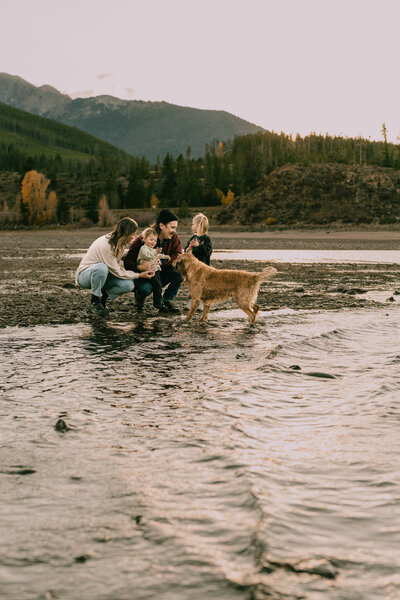 Candid photo of family playing with dog by lake