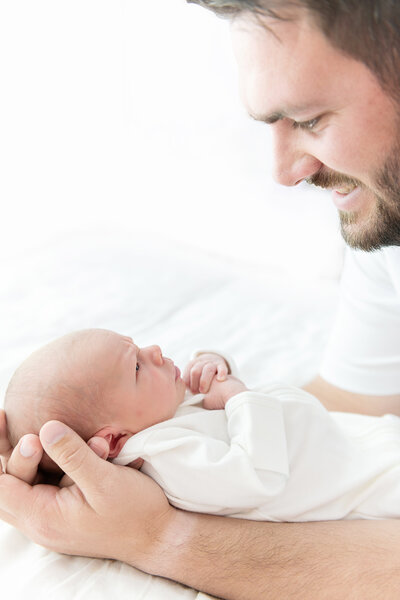 A happy father smiles down at his newborn baby awake in his hands posed by a Atlanta newborn photographer