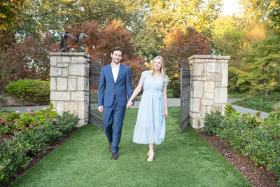 Young man and woman walk through park gates during their engagement photography session