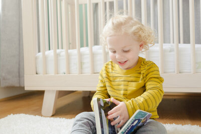 Boy sitting on nursery floor reading a book smiling - Family Photographer Nashville