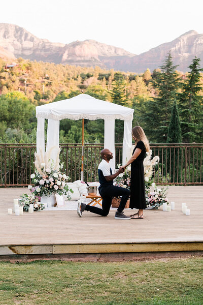 Man proposing to a woman with the mountains in the background and a picnic set up