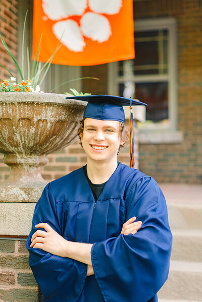 High school senior guy wearing a navy blue cap and gown and posing in front of a Clemson flag