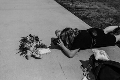 Woman laying on her stomach photographing flowers at wedding