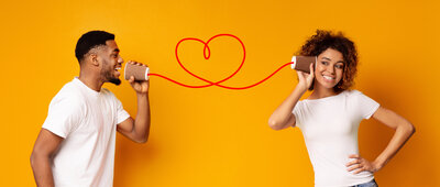 Black couple communicating with phone cups linked with heart shaped cord.
