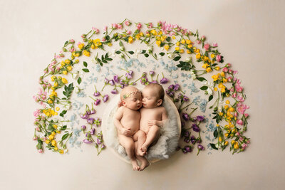 newborn twin babies cuddling close together surrounded by florals in the design of a rainbow