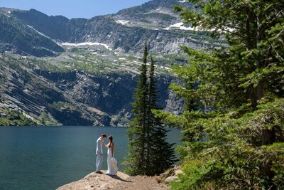 A bride and groom stand in the wilderness next to an alpine lake in Montana.