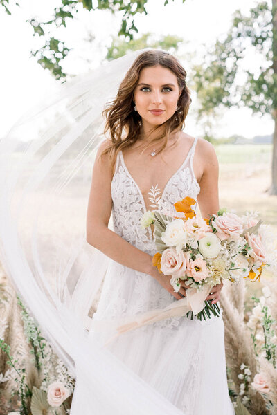 A beautiful bride holding a bouquet. Her wedding veil is swinging out around her and her dress is all lace