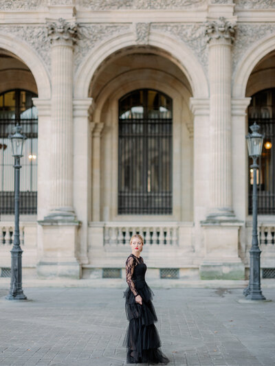 a woman in a black tulle dress standing in between two light posts at the louvre in paris