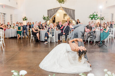 A groom dips his bride during their first dance at their wedding reception.