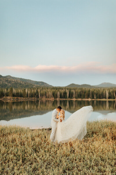 bride and groom kissing in a field with mountains behind them