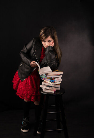 tween-girl-reader-with leather-jacket-looking-at-stacked-books