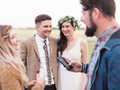 Man holds phone while talking with bride and groom